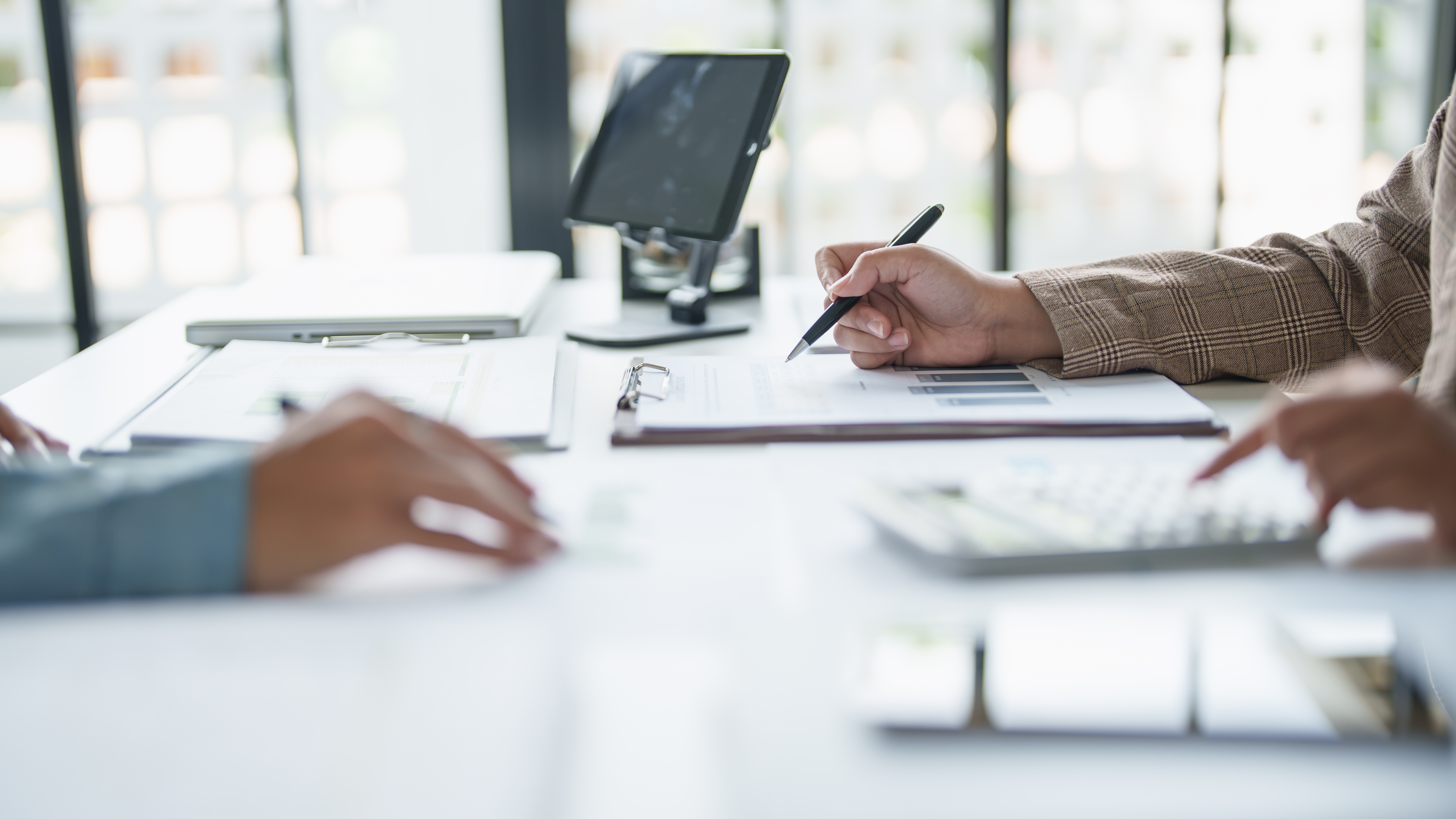 Close-up of professionals reviewing documents and taking notes during a meeting in an office environment.