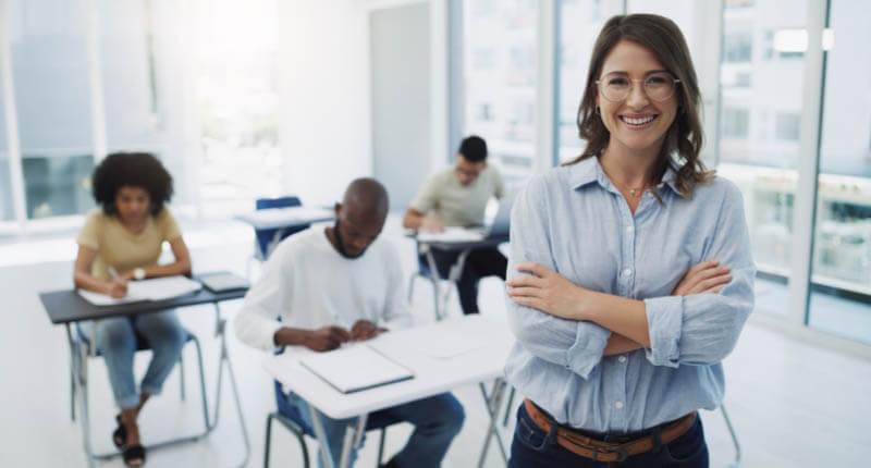 Education, portrait and woman professor in a classroom with students for teaching, knowledge and motivation. College, teacher and face of female leader happy in a class with group of people learning