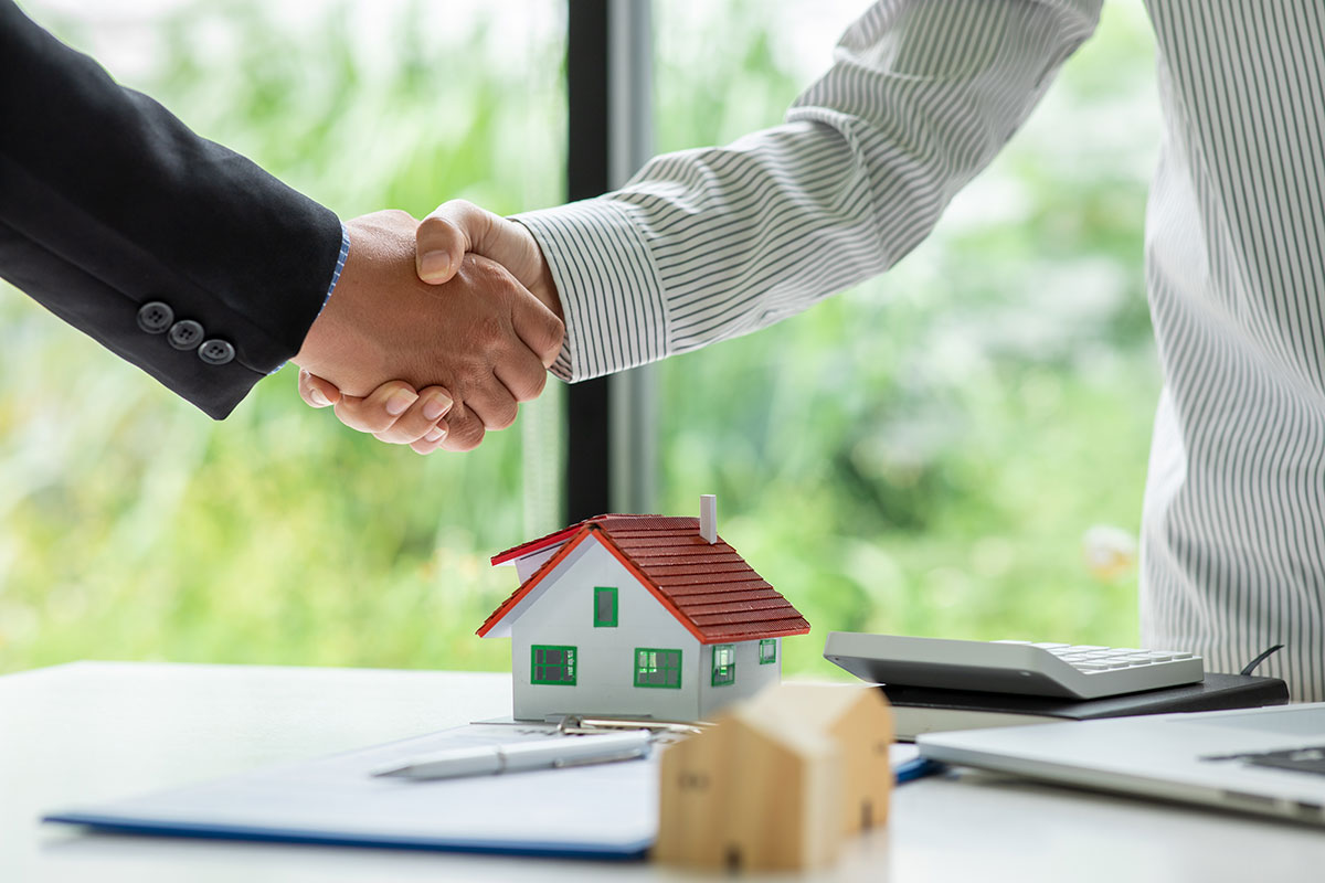 Realtor and client shake hands over mini house
