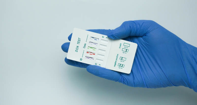 Holds a drug test kit to find out five types of drugs in the body through urine. wearing medical gloves and holding a drug test kit, isolated on white