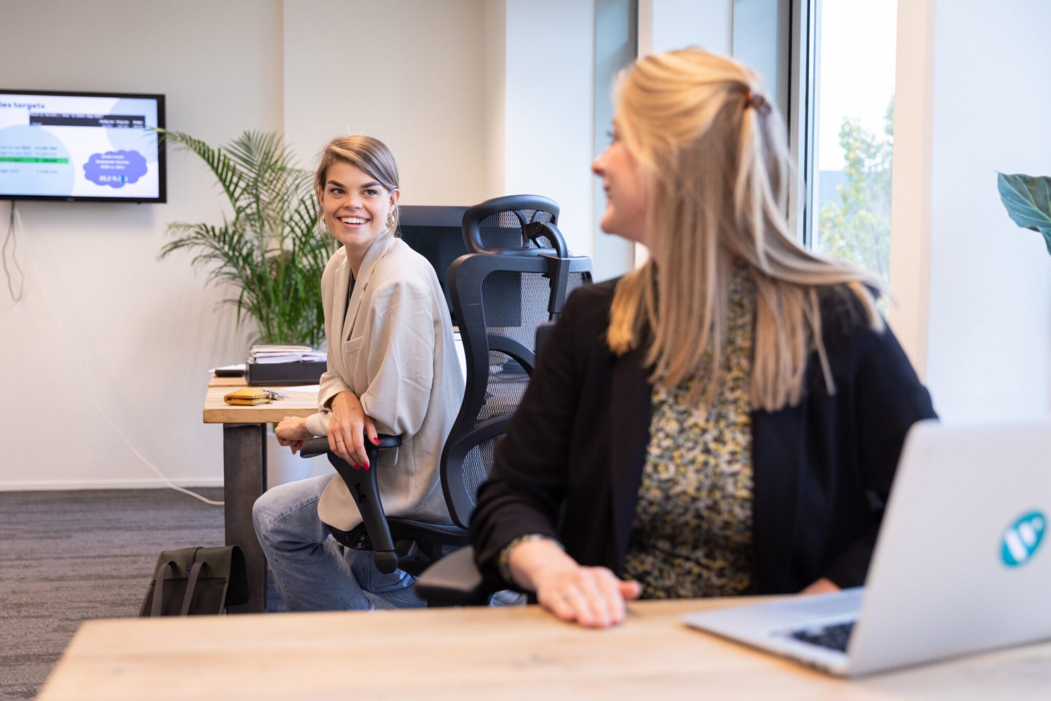 Two colleagues are sitting at their desks conversing with each other.
