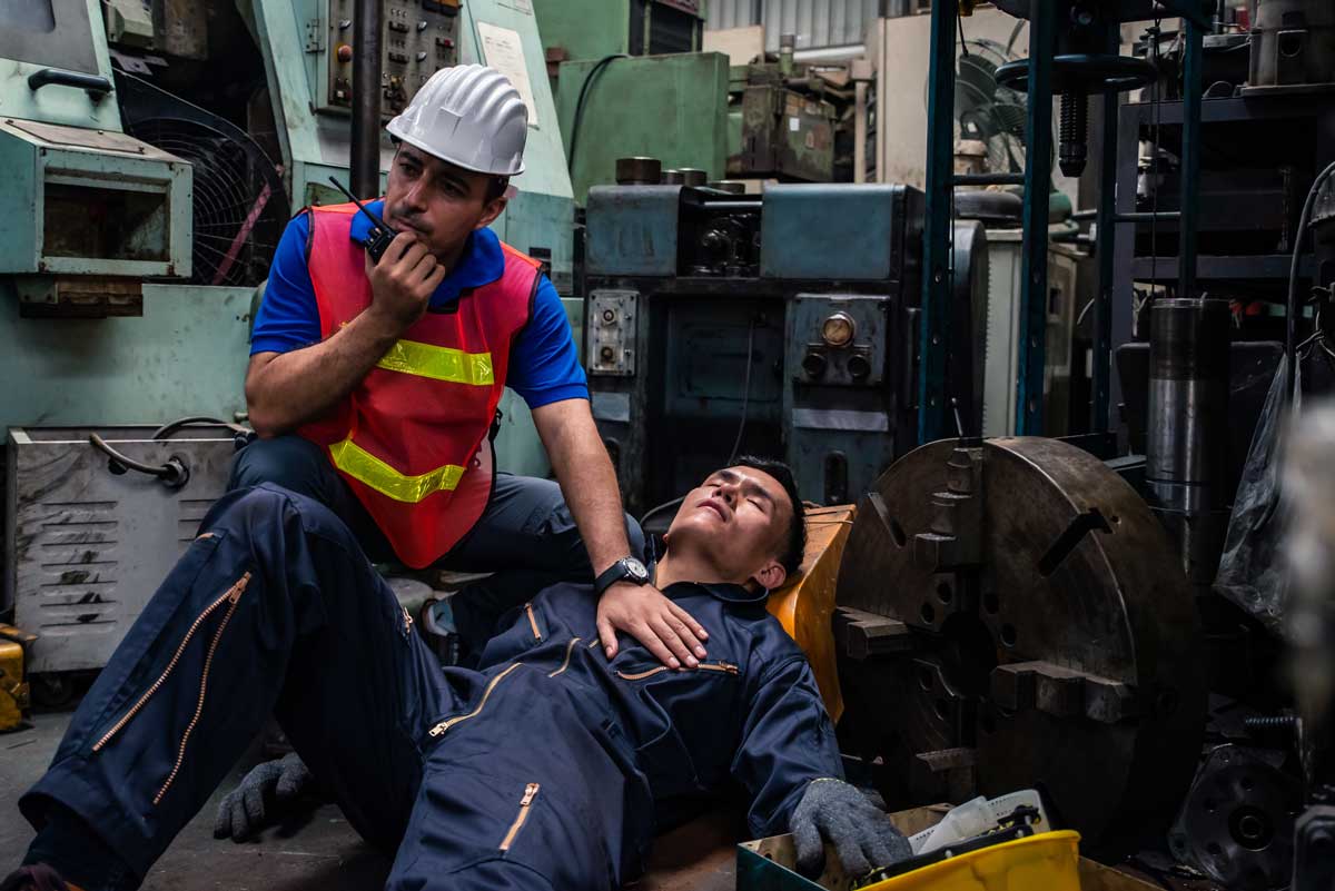 Worker had accident unconscious on the floor at factory. Male engineer supervisor talking on walkie talkie for help. Safety in Factory industrial and drug testing concept.